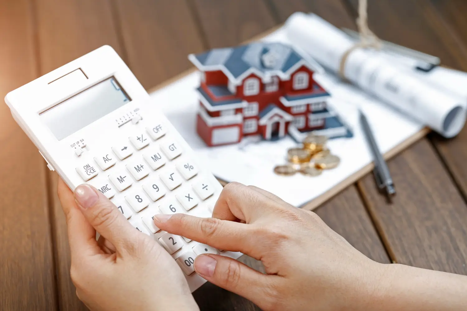 Mulher utilizando uma calculadora com uma pequena casa ao fundo acima da mesa, representando o valor venal do imóvel